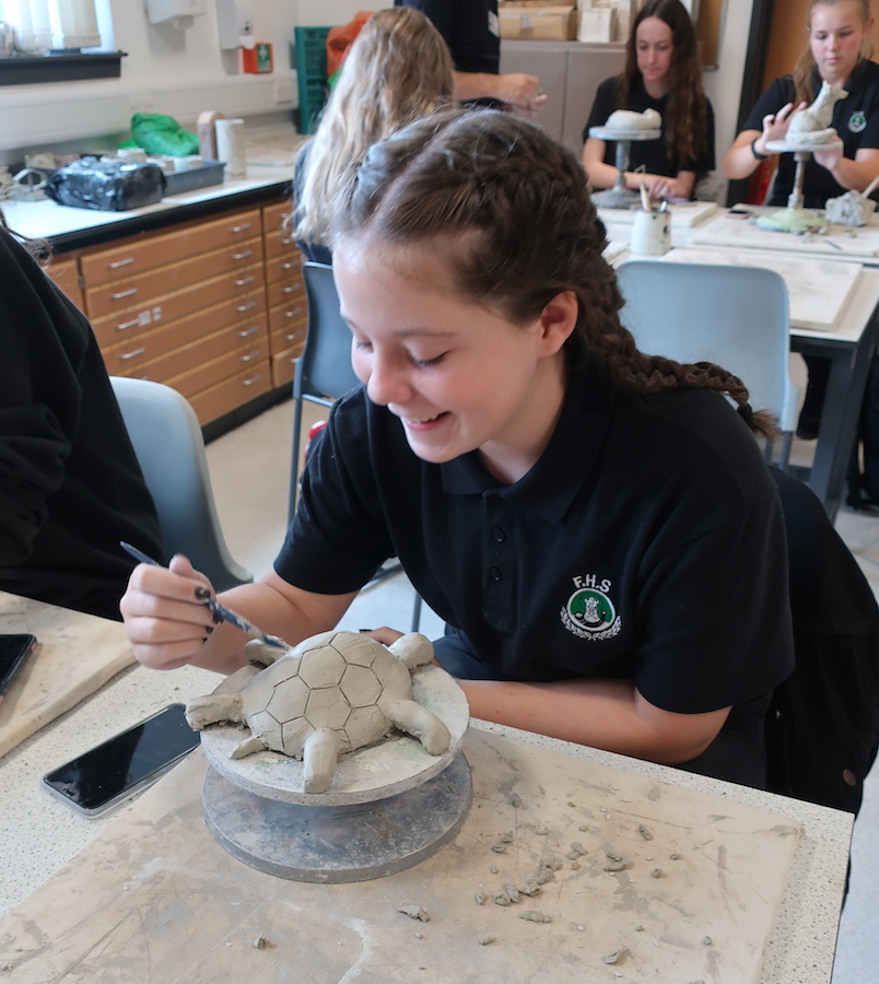 Student adding details to their clay animal sculpture