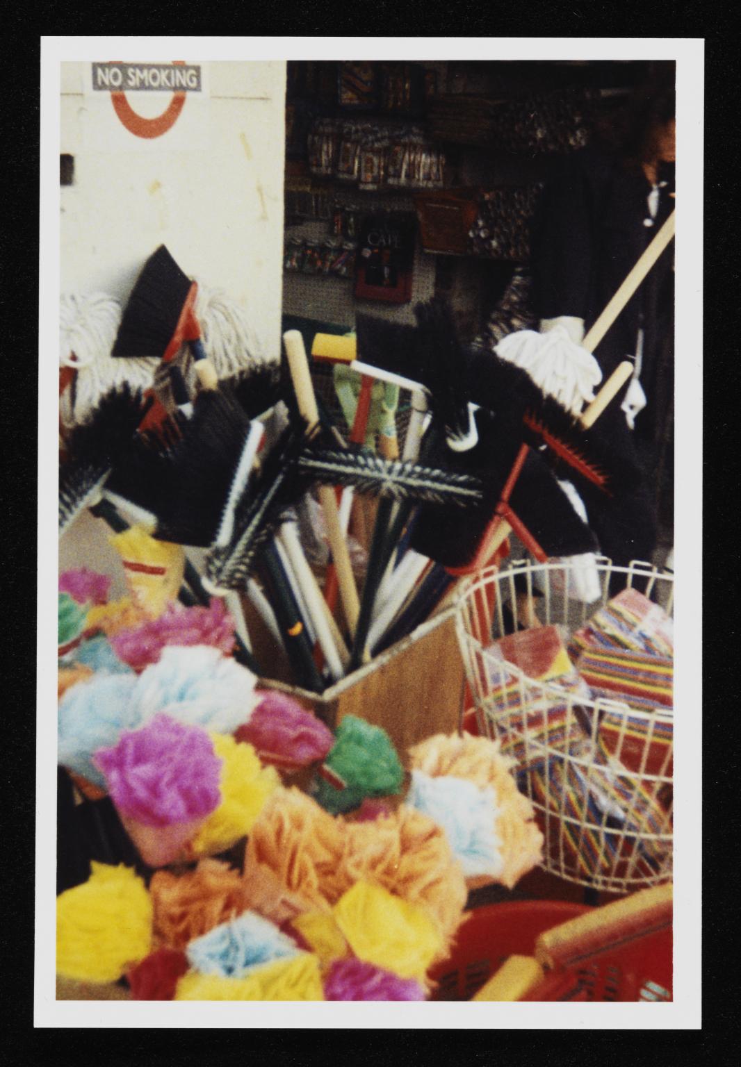 Plastic flowers, brooms, and sponges in boxes and buckets outside a shop
