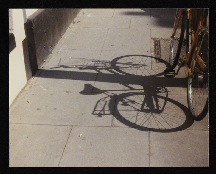 Colour photograph of the shadow of a bicycle on the pavement 