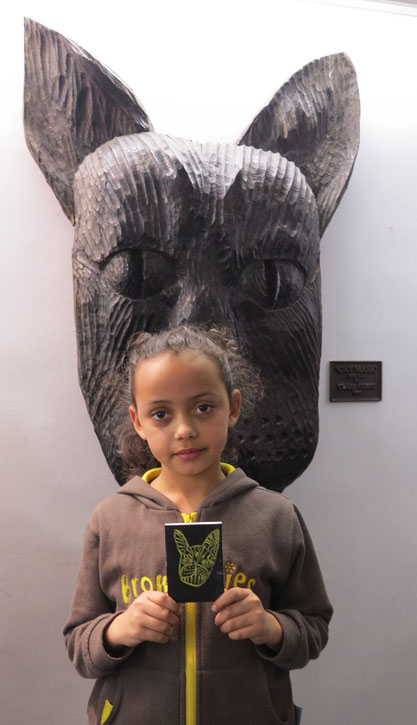 A Harlow Brownie with her drawing of the 'Cat Mask (1)' sculpture behind her