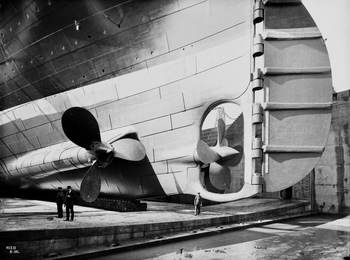Triple propeller arrangement and rudder, portside view from dock floor, with three figures