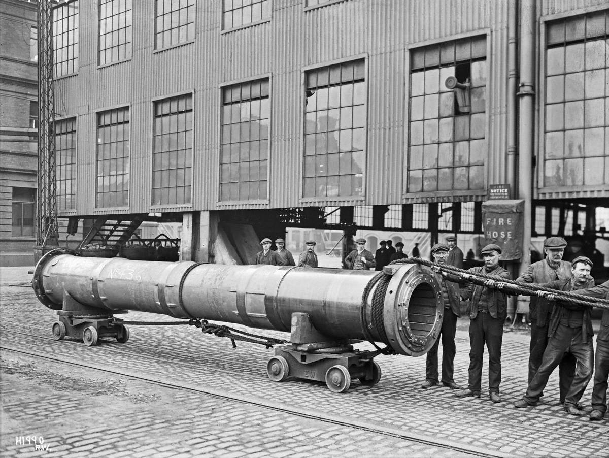 Tail shaft on two narrow gauge rail buggies being hauled by squad of men outside works