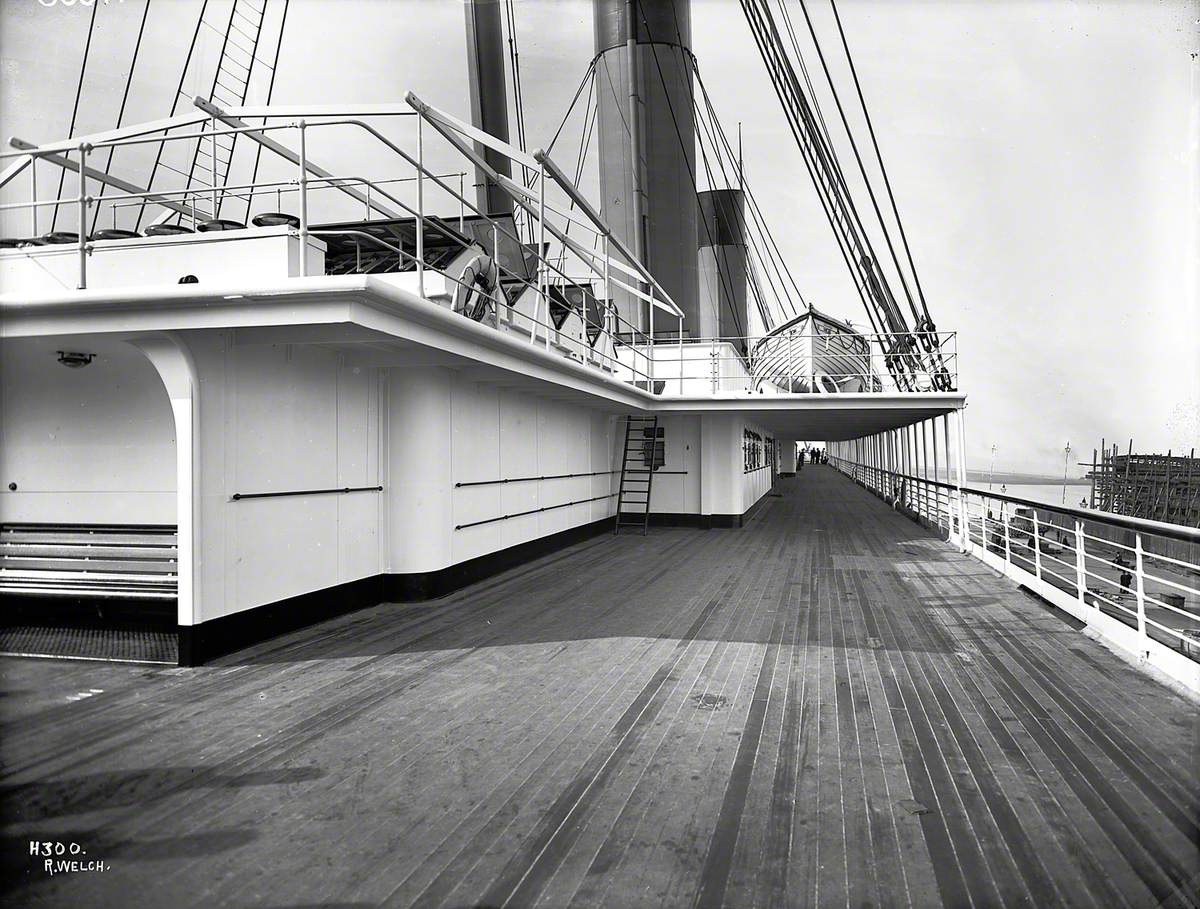 View forward along starboard promenade deck including funnels and boat deck