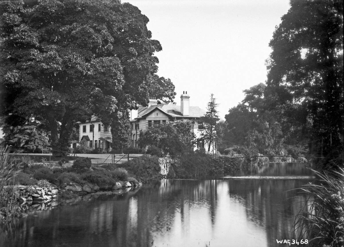 Untitled (a side view of a large mansion, beside a river with a weir)