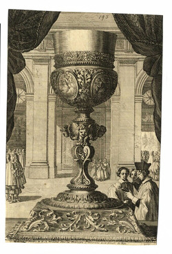 A monumental silver chalice placed on a pedestal with heads and floral decorations, surrounded by figures