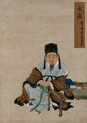 A Seated Chinese Figure with Arm Resting on a Table with Books, Wearing Brown and Pale Blue Robes and Tall Black Hat