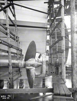 Close-up of portside propeller, with shipwright standing on adjacent staging