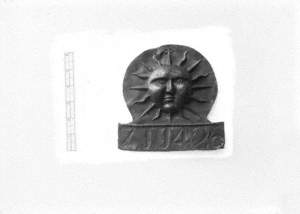 Untitled (a view of a sun face plaque on a white background with scale)