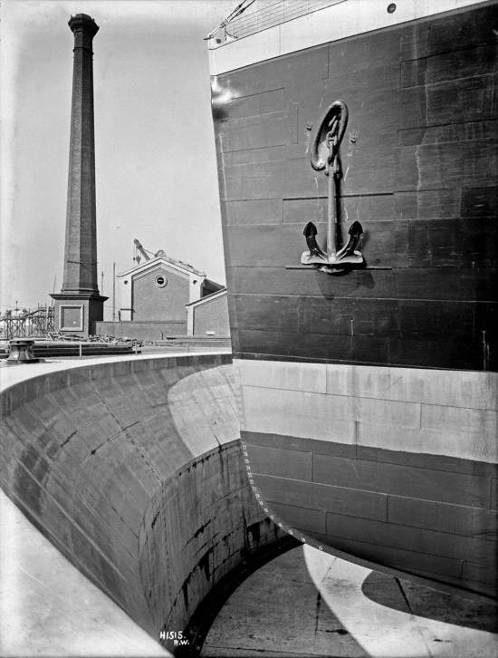 Port bow profile from side of graving dock with pump house and chimney in background