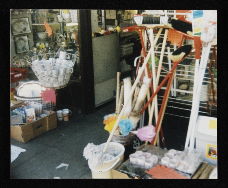 Colour photograph of brooms, mugs, dusters, and other merchandise arranged outside a shop