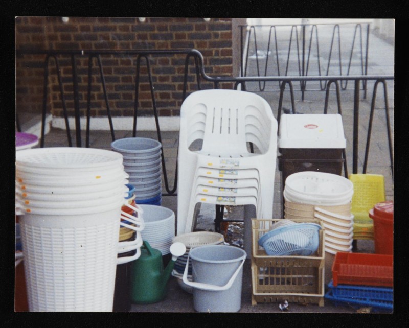 Colour photograph of plastic chairs, bins, buckets and baskets stacked up outside