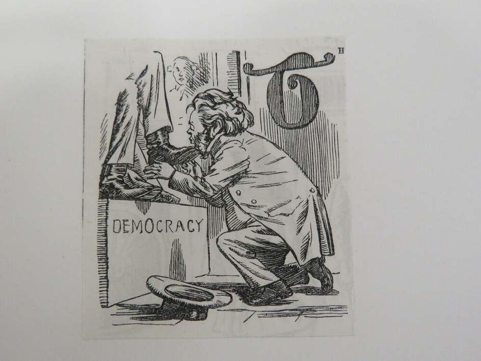 Kneeling man kissing the boot of a man on a podium labelled democracy, with a letter T in the background